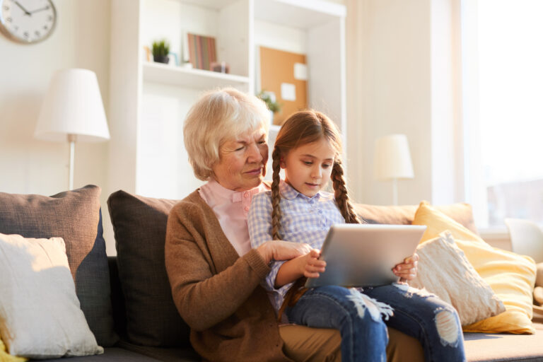 Portrait of grandmother reading stories to cute little girl using digital tablet together, copy space